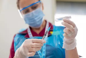 Nurse wearing full personal protective equipment, holding a syringe.